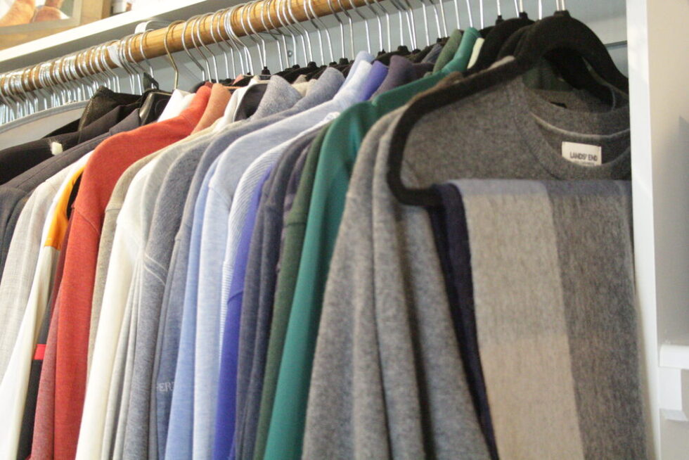 Row of colorful clothing garments hanging on hangers inside a wardrobe